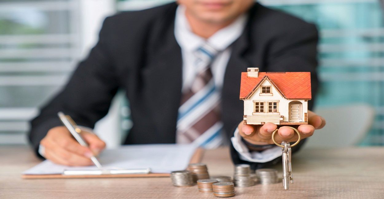 Person in a suit holding a model house and keys